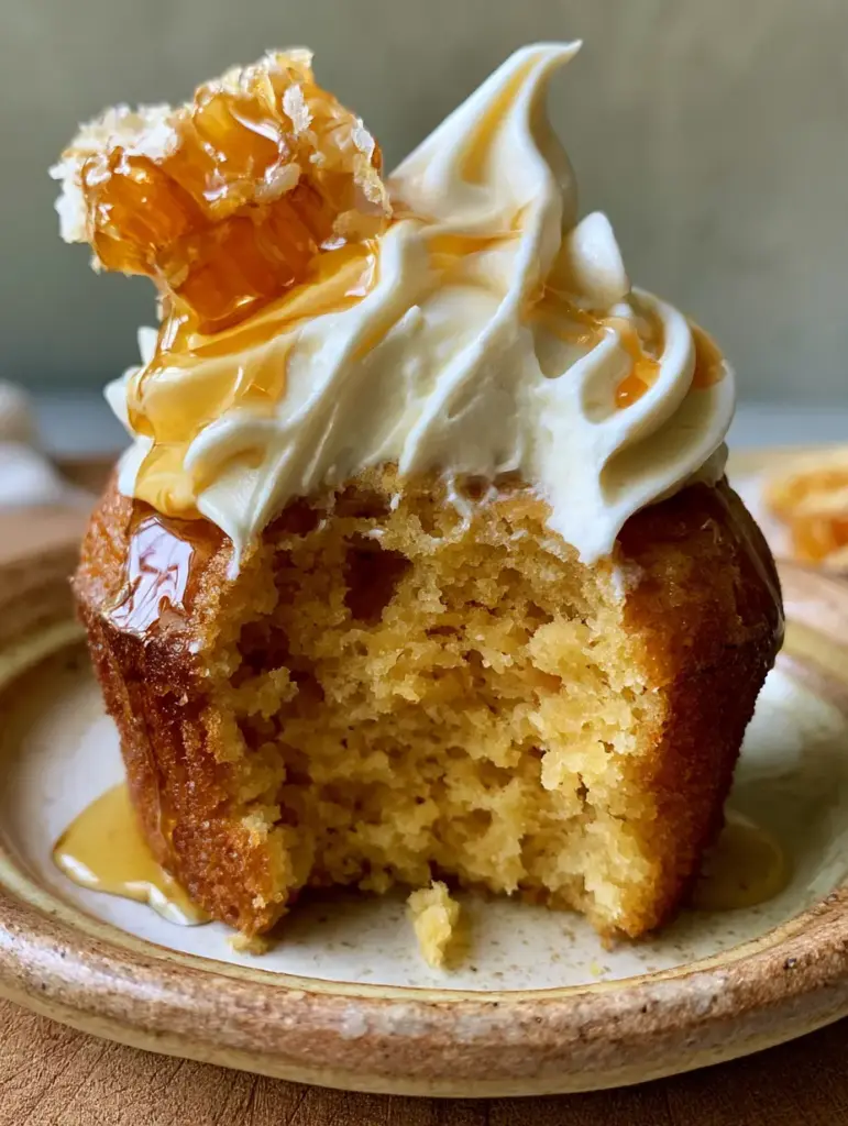 Honey Cupcakes with Whipped Honey Buttercream and Fresh Honeycomb 1 Top-down view of honey cupcakes on a ceramic plate, showing the velvety swirl of buttercream and fresh honeycomb garnish.