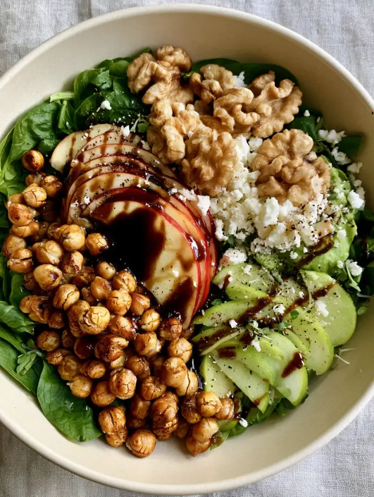 Close up of glossy maple balsamic glaze drizzled over a spinach apple chickpea salad with micro-herb garnish.