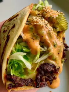 A hyper-realistic close-up of a seared ground beef layer with charred edges inside a Big Mac Wrap.