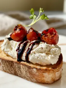 Macro shot of a sourdough crostini topped with swirling whipped feta and bursting cherry tomatoes. (appetizer recipe)