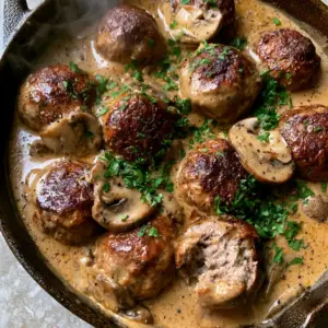 Top-down view of perfectly seared beef meatballs in a golden-brown mushroom sauce in a cast iron pan. (meatballs in mushroom sauce)
